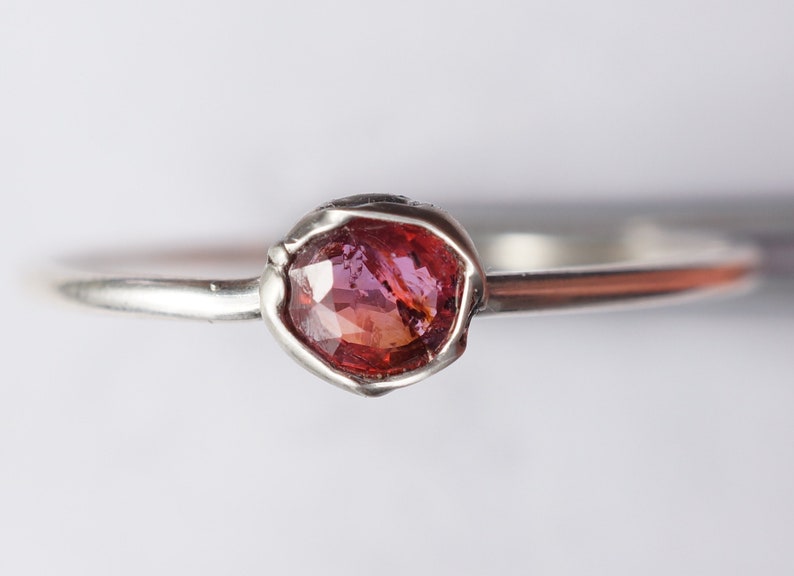 Op de afbeelding: Een zilveren ring met een roze en rode edelsteen in een bezel-setting.