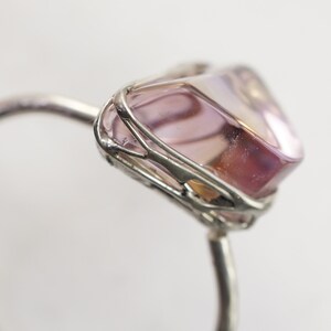 May include: A silver ring with a pink and purple gemstone set in a wire cage.