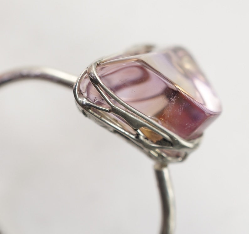 May include: A silver ring with a pink and purple gemstone set in a wire cage.