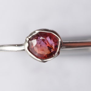 Op de afbeelding: Een zilveren ring met een roze edelsteen gezet in een ruwe, getextureerde zetting.