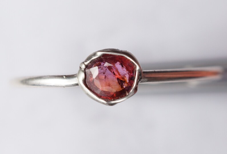 Op de afbeelding: Een zilveren ring met een roze edelsteen gezet in een ruwe, getextureerde zetting.