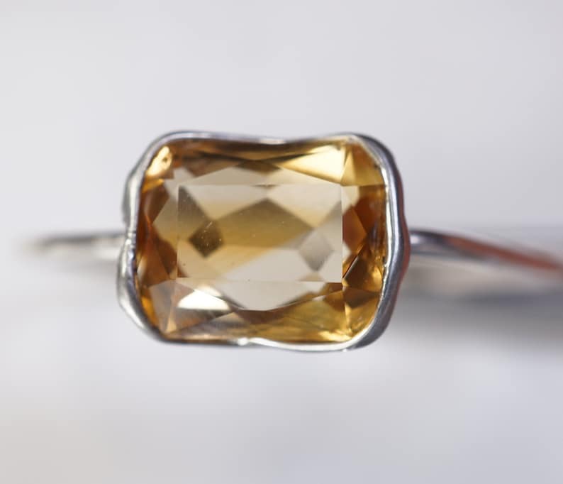 May include: A silver ring with a large, rectangular, light brown gemstone.