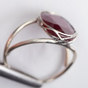 May include: A silver ring with a large, oval-shaped, dark red gemstone set in a delicate, openwork design.