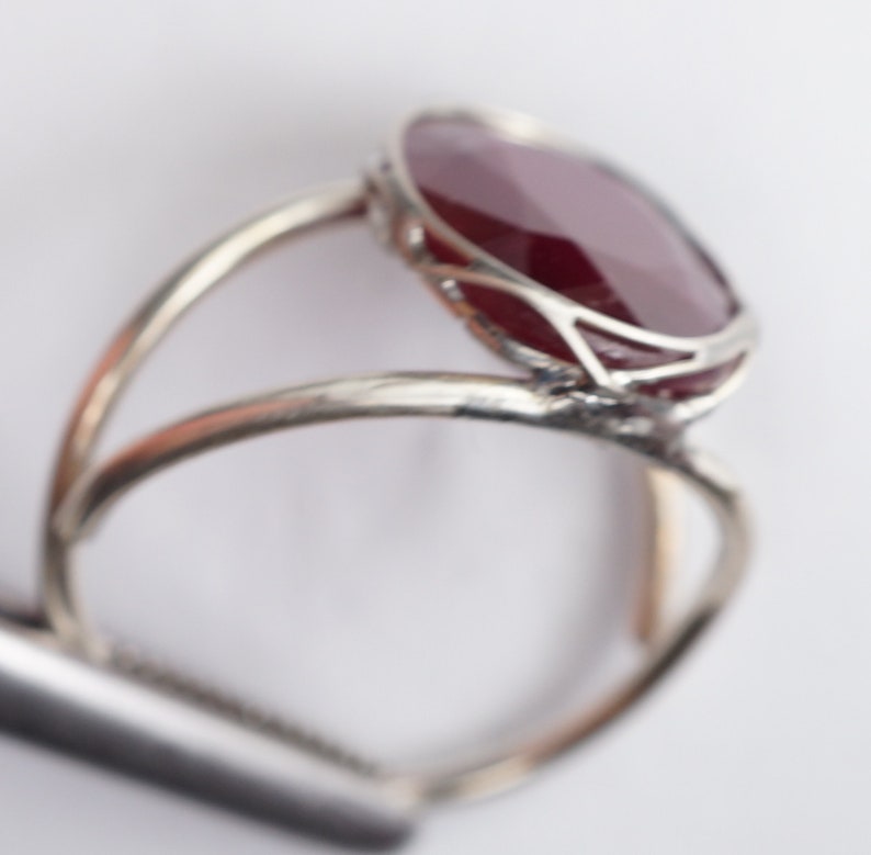 May include: A silver ring with a large, oval-shaped, dark red gemstone set in a delicate, openwork design.