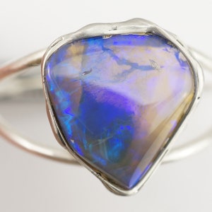 May include: A silver ring with a large, blue, iridescent opal gemstone set in a rough, irregular shape.