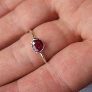 Pode incluir: Um anel de prata com uma gema de rubi vermelho engastada em uma moldura.