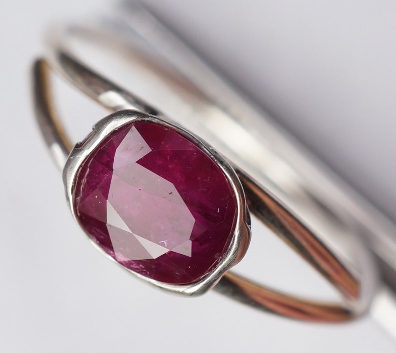 Op de afbeelding: Een zilveren ring met een grote, gefacetteerde robijn. De robijn is diep rood van kleur en is gezet in een bezel setting.