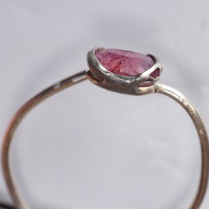 May include: A silver ring with a pink gemstone set in a delicate, open-work setting.