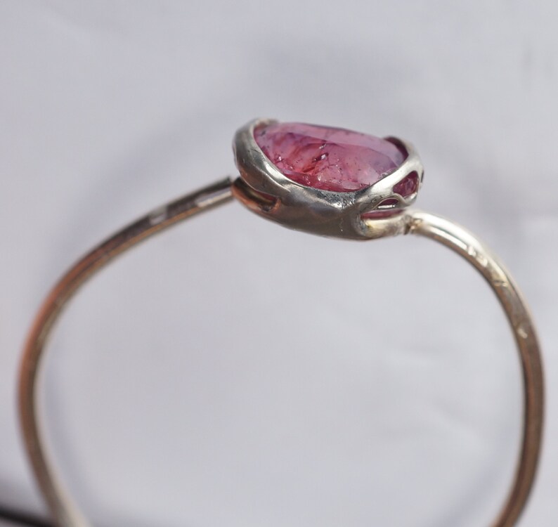 May include: A silver ring with a pink gemstone set in a delicate, open-work setting.