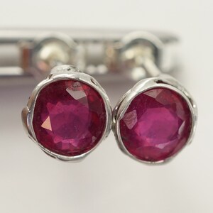 May include: A pair of silver stud earrings with round, faceted ruby gemstones.