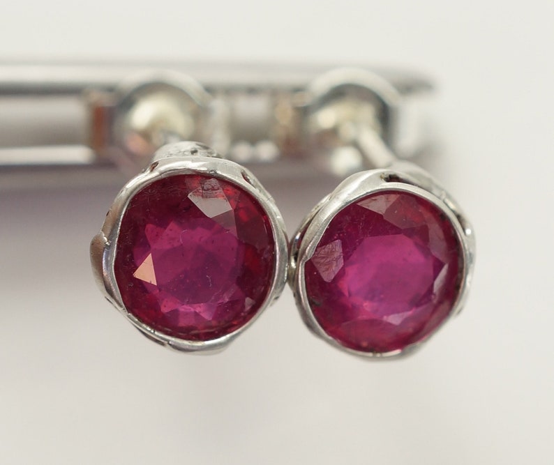 May include: A pair of silver stud earrings with round, faceted ruby gemstones.