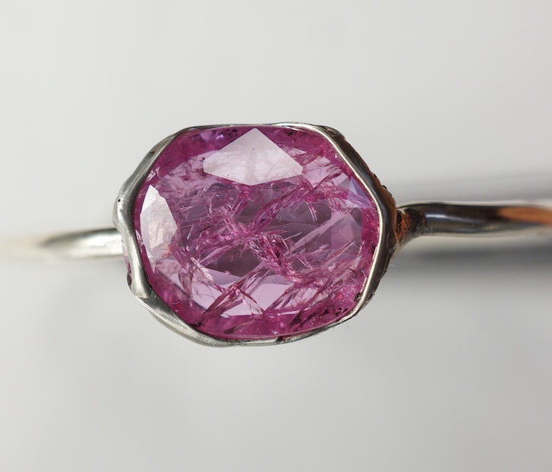 May include: A silver ring with a large, faceted, pink gemstone set in a bezel setting.