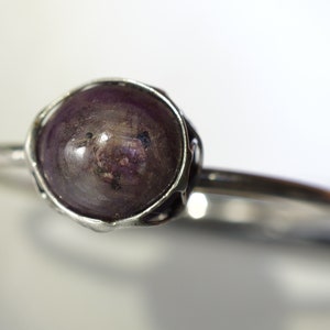 May include: A silver ring with a dark purple gemstone set in a wire-wrapped bezel.