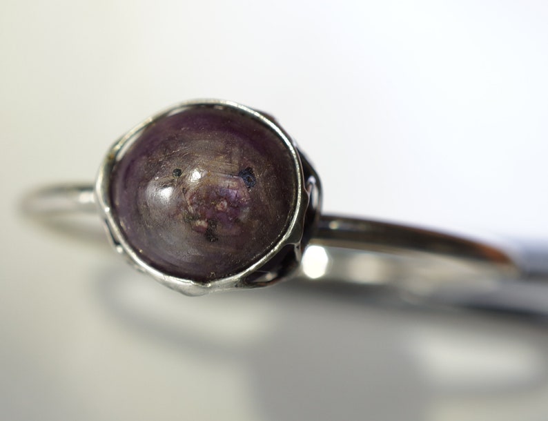 May include: A silver ring with a dark purple gemstone set in a wire-wrapped bezel.