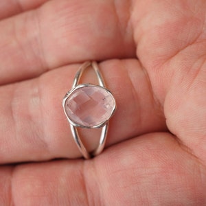 Puede incluir: Un anillo de plata con un dise&ntilde;o delicado presenta una piedra preciosa ovalada de color rosa p&aacute;lido.