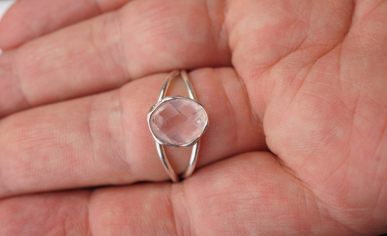 Puede incluir: Un anillo de plata con un dise&ntilde;o delicado presenta una piedra preciosa ovalada de color rosa p&aacute;lido.