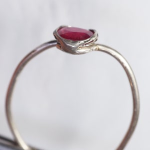 May include: A silver ring with a red gemstone set in a textured band.