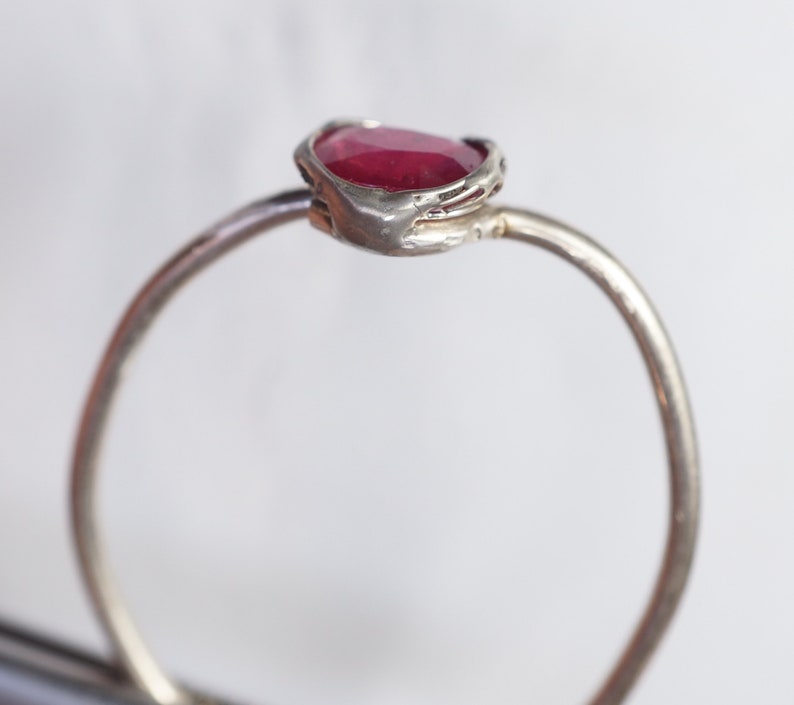 May include: A silver ring with a red gemstone set in a textured band.