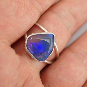 May include: A silver ring with a blue opal gemstone set in a bezel setting. The ring has a twisted band.
