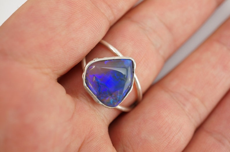 May include: A silver ring with a blue opal gemstone set in a bezel setting. The ring has a twisted band.