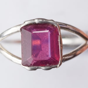 May include: A silver ring with a large, deep pink, emerald-cut gemstone.