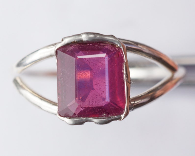 May include: A silver ring with a large, deep pink, emerald-cut gemstone.