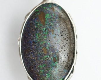 May include: A silver pendant with a large oval opal stone. The opal has a dark gray base with green and blue iridescent flashes.