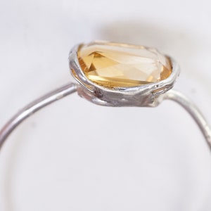 May include: A silver ring with a large, faceted, yellow gemstone set in a textured silver bezel.
