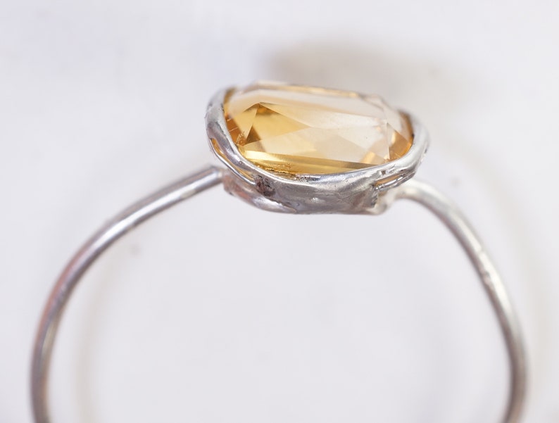 May include: A silver ring with a large, faceted, yellow gemstone set in a textured silver bezel.