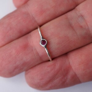 Puede incluir: Un anillo de plata con una peque&ntilde;a piedra preciosa redonda de color rosa oscuro engastada en un engaste de bisel.