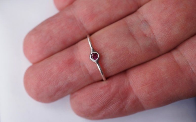 Puede incluir: Un anillo de plata con una peque&ntilde;a piedra preciosa redonda de color rosa oscuro engastada en un engaste de bisel.