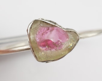 Può includere: Un anello d'argento con una pietra preziosa rosa e verde incastonata in una forma grezza e naturale.