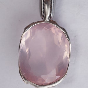 May include: A pale pink rose quartz pendant with a silver setting. The pendant is oval shaped and has a smooth, polished surface.