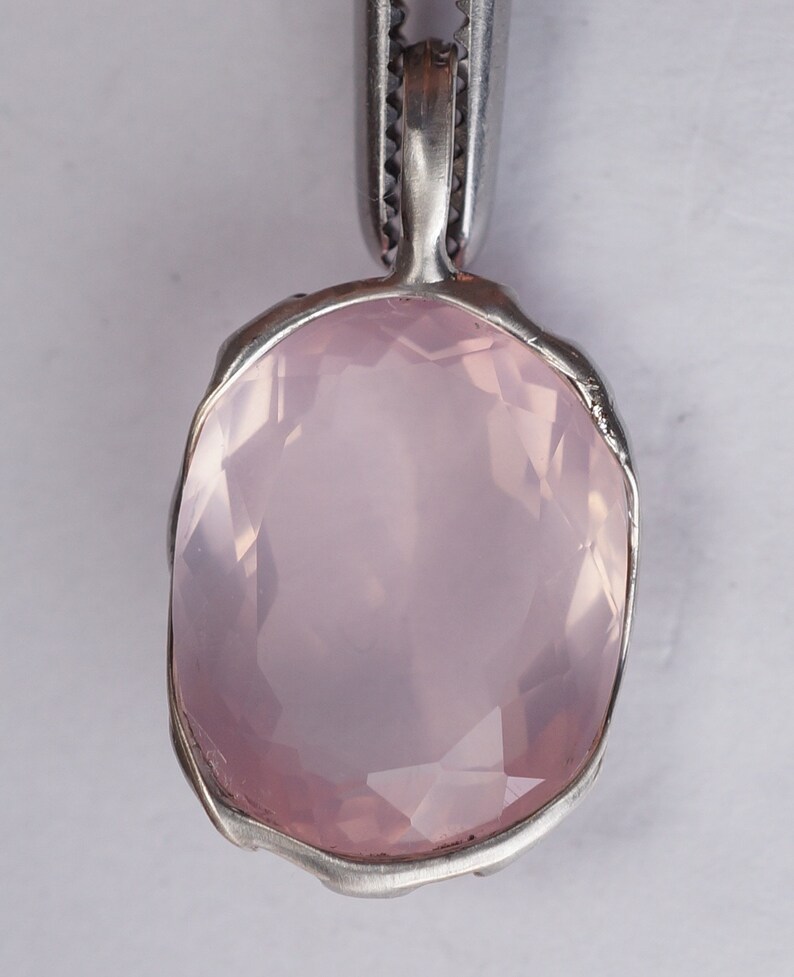 May include: A pale pink rose quartz pendant with a silver setting. The pendant is oval shaped and has a smooth, polished surface.