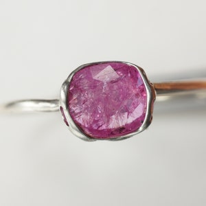 Op de afbeelding: Een zilveren ring met een roze edelsteen gezet in een bezel setting. De edelsteen is gefacetteerd en heeft een ruwe, natuurlijke uitstraling.