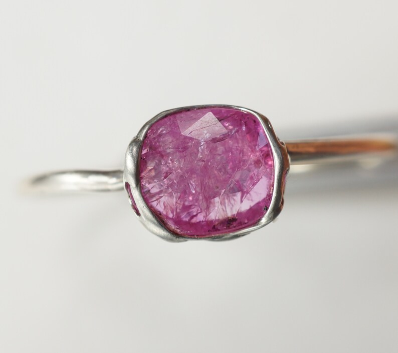 Op de afbeelding: Een zilveren ring met een roze edelsteen gezet in een bezel setting. De edelsteen is gefacetteerd en heeft een ruwe, natuurlijke uitstraling.