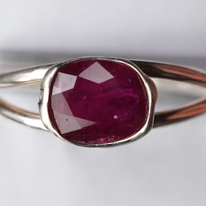 Op de afbeelding: Een zilveren ring met een diep rode, gefacetteerde edelsteen in een bezel-setting.