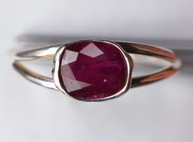 Op de afbeelding: Een zilveren ring met een diep rode, gefacetteerde edelsteen in een bezel-setting.