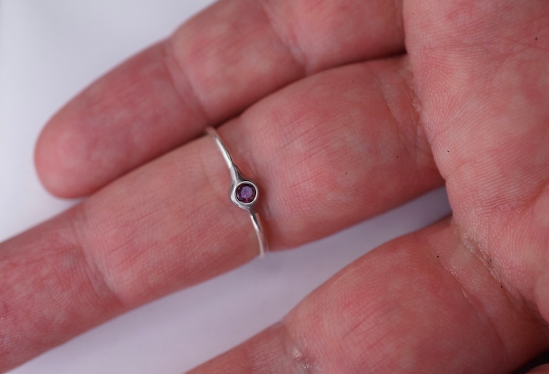 Puede incluir: Un anillo de plata con una peque&ntilde;a piedra preciosa redonda de color p&uacute;rpura.