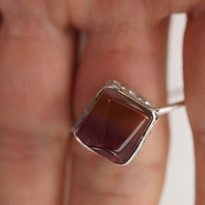 Op de afbeelding: Een zilveren ring met een vierkante, bruine en paarse edelsteen.