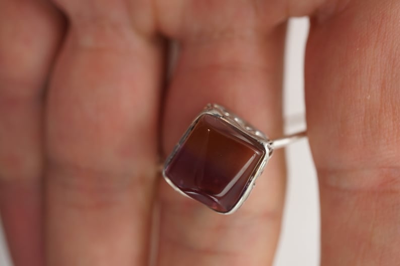 Op de afbeelding: Een zilveren ring met een vierkante, bruine en paarse edelsteen.