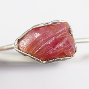 May include: A silver ring featuring a raw pink ruby gemstone. The ruby is set in a wire-wrapped design.