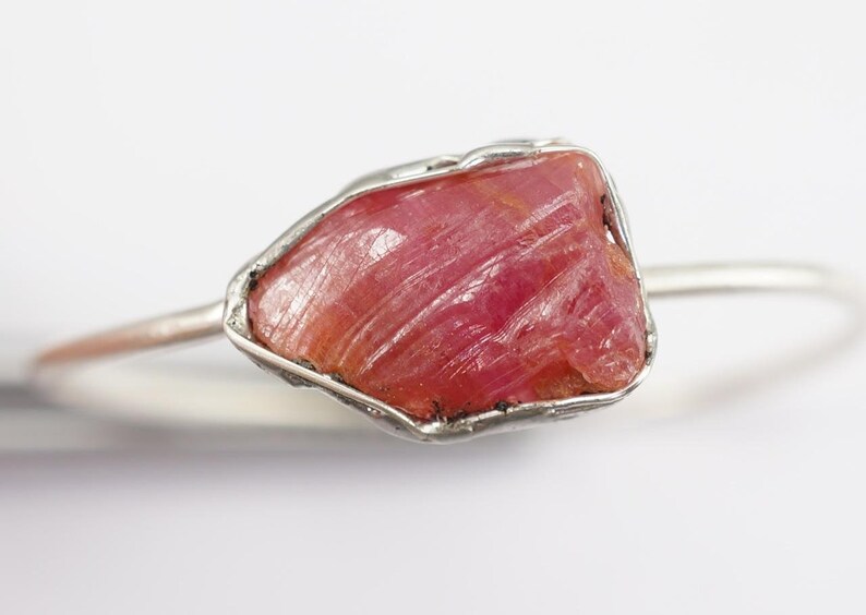 May include: A silver ring featuring a raw pink ruby gemstone. The ruby is set in a wire-wrapped design.