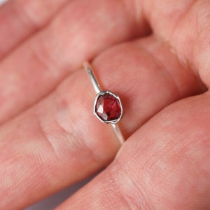 Op de afbeelding: Een zilveren ring met een rode edelsteen in een bezel-setting.