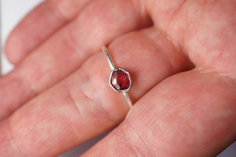 Op de afbeelding: Een zilveren ring met een rode edelsteen in een bezel-setting.