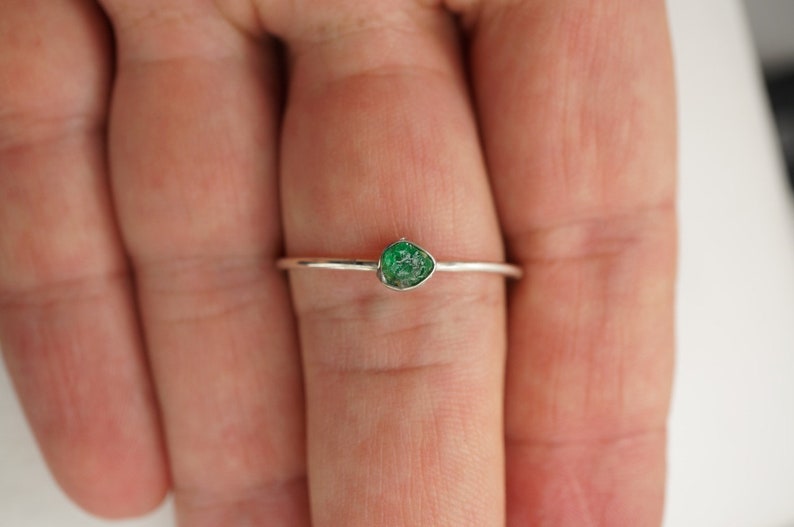 Peut inclure: Une bague en argent avec une petite pierre pr&eacute;cieuse verte sertie au centre.