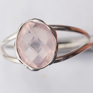 Puede incluir: Un anillo de plata con una piedra preciosa de cuarzo rosa. El anillo tiene una banda delicada y retorcida.