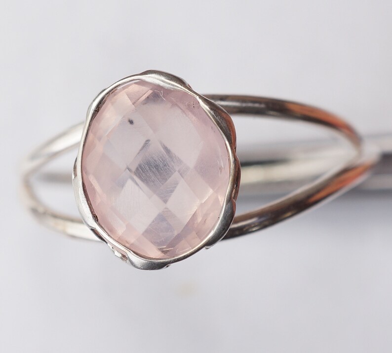 Puede incluir: Un anillo de plata con una piedra preciosa de cuarzo rosa. El anillo tiene una banda delicada y retorcida.