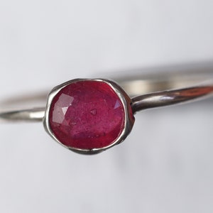 May include: A silver ring with a deep red ruby gemstone set in a textured bezel.