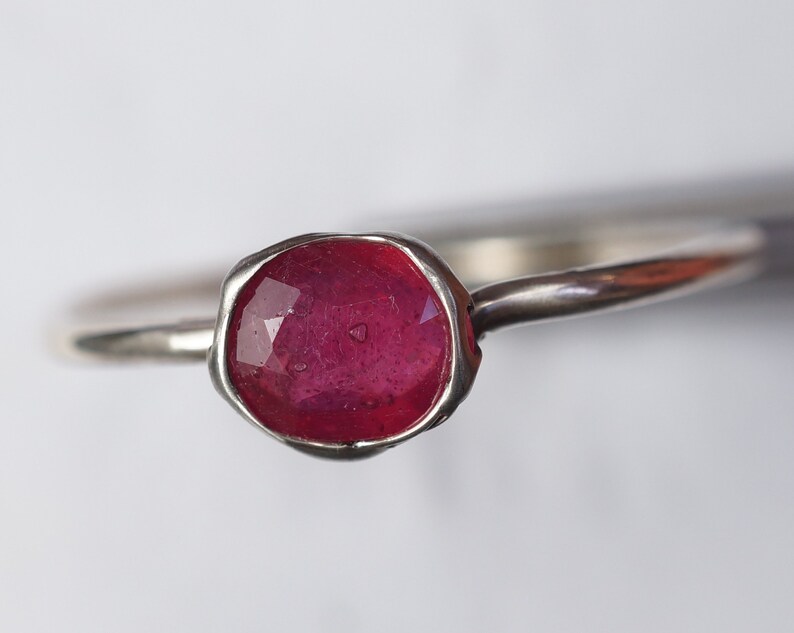 May include: A silver ring with a deep red ruby gemstone set in a textured bezel.